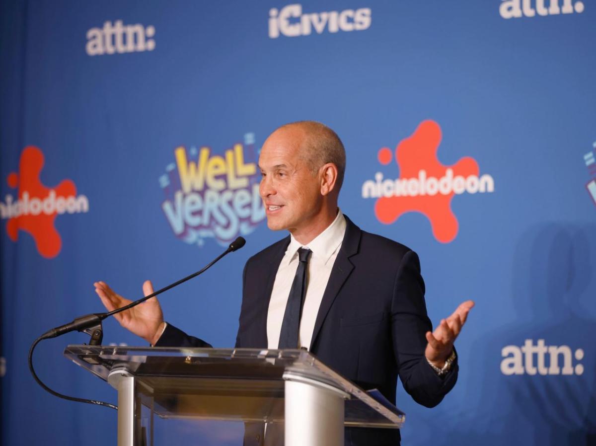 A speaker stood at a stand, talking into a microphone at the “Well Versed” premiere