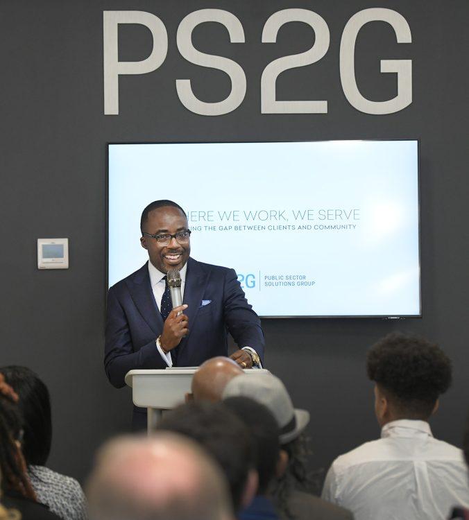 Person stood infront of a crowd, holding a microphone with a screen behind them