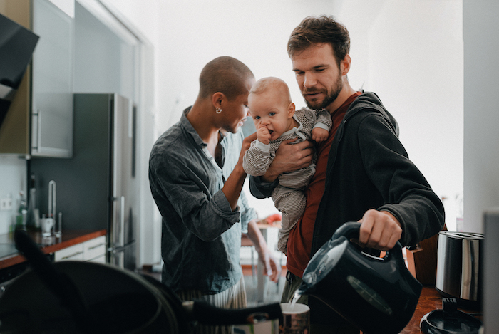 Two male parents getting ready for work in the morning and holding their son.