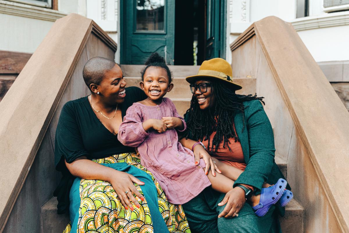 Two smiling Black women sitting on front stoop with a young, smiling Black girl