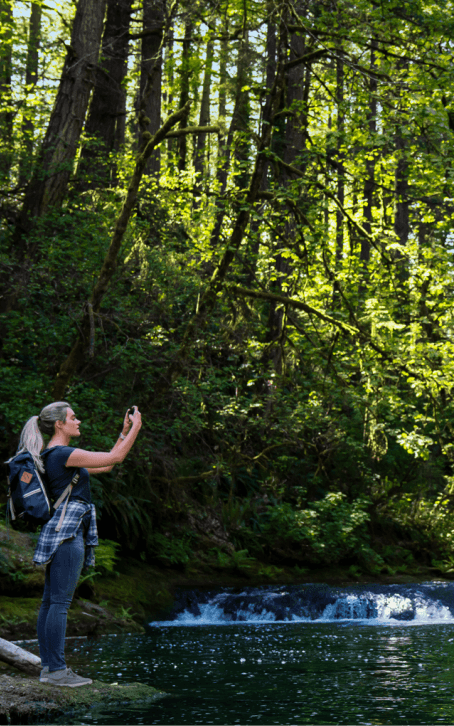 hiker taking a picture of a stream and trees