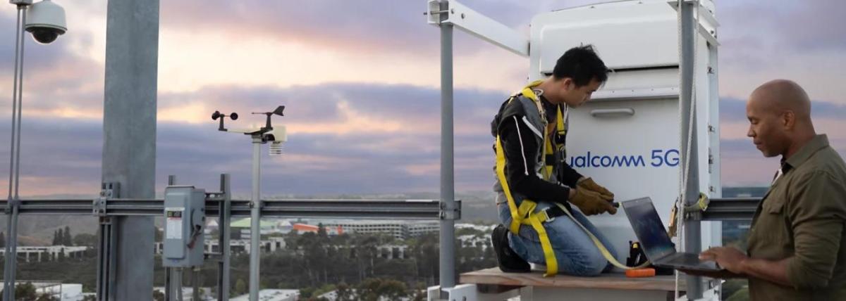 People working on top of a building in front of a Qualcomm 5G device