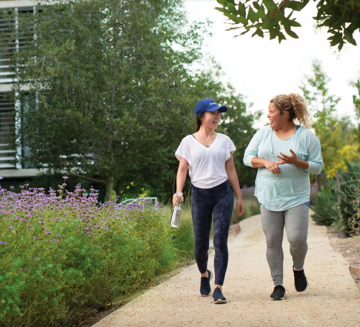 Two people walking on a path together, talking. Lush plants to the sides.