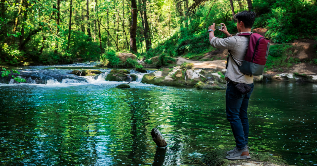 Person standing on a riverbank taking a picture of the water