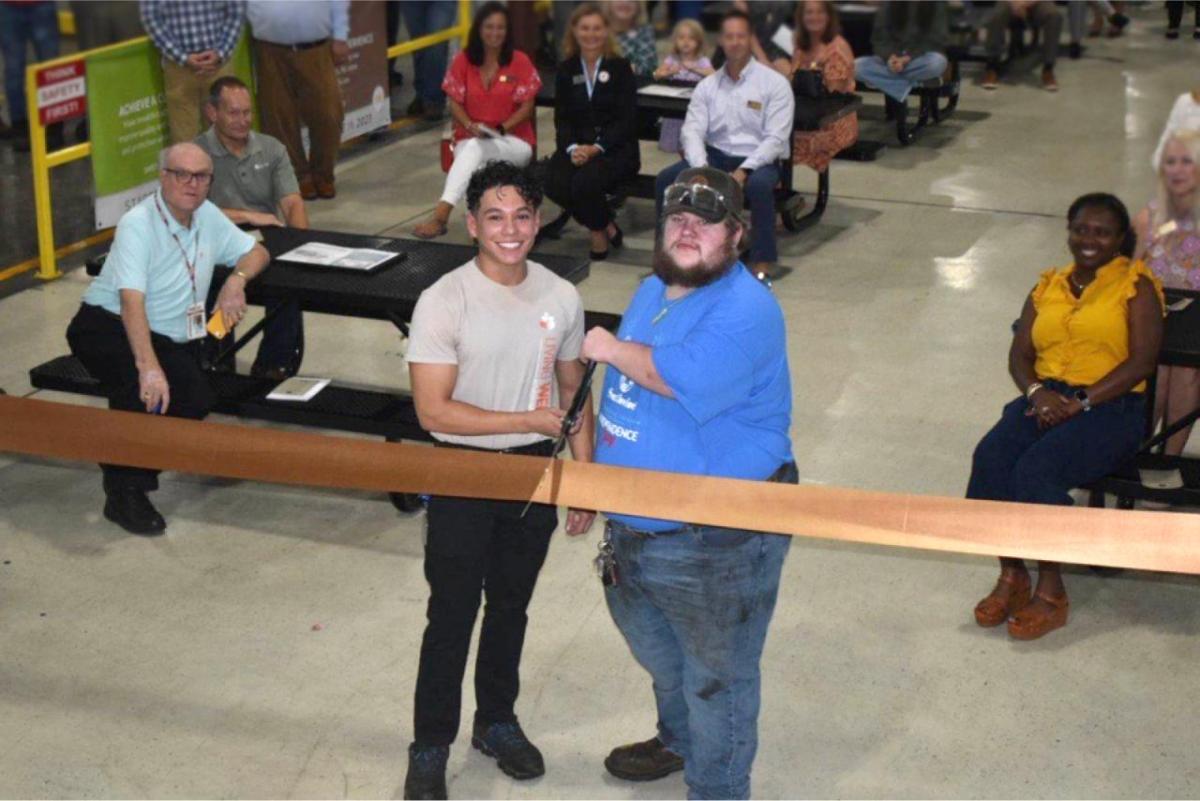 Two people cutting the ribbon in front of people sat on benches