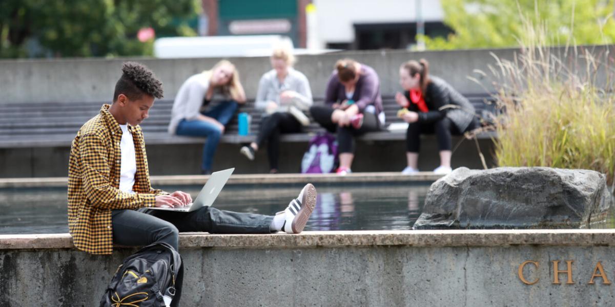 Student sat on a wall using their laptop 