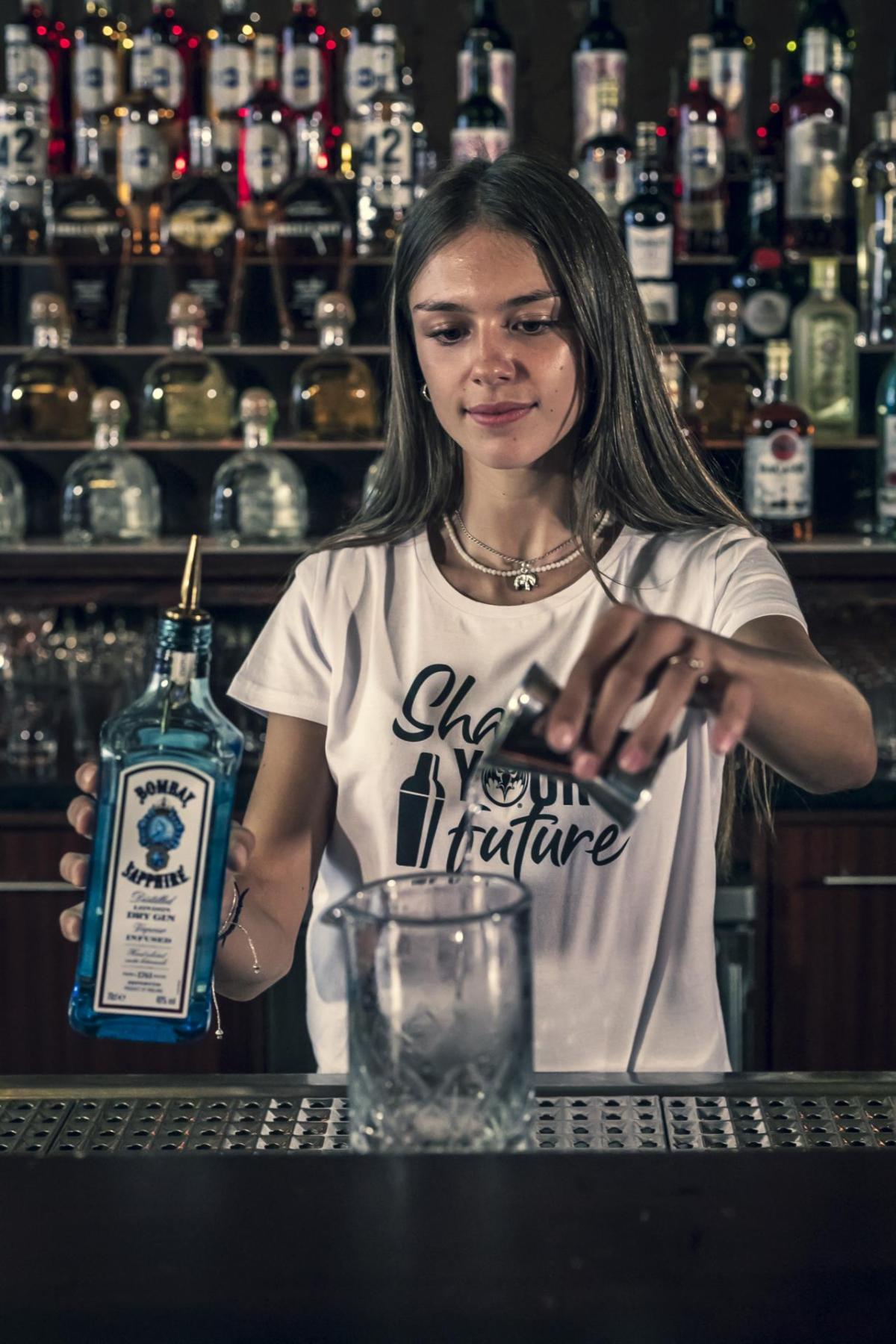A bartender training  student pouring alcohol into a glass