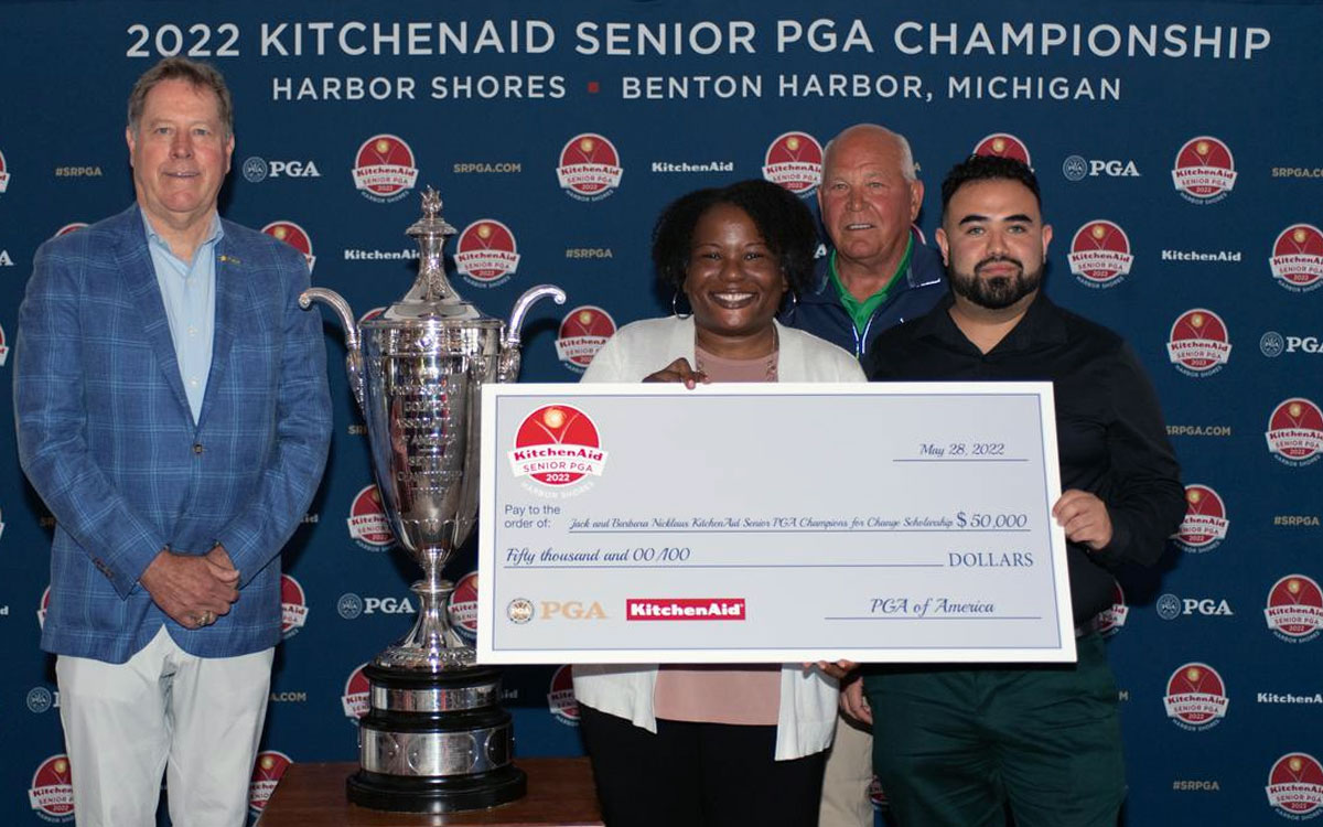 Both scholarship winners stand with the PGA trophy and a large check next to the two presenters