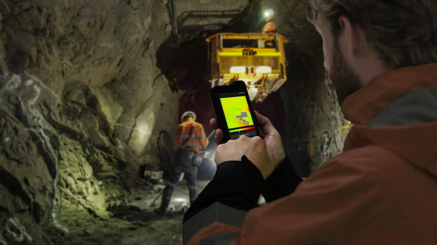 Several workers inside a mine. In the foreground one worker is using a phone.