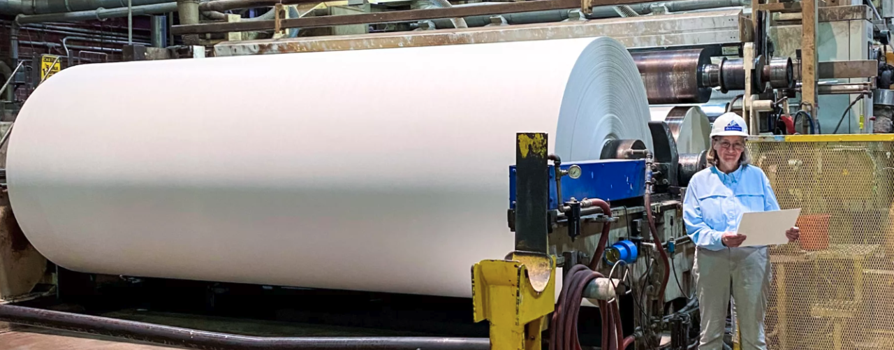 Worker standing next to giant paper roller