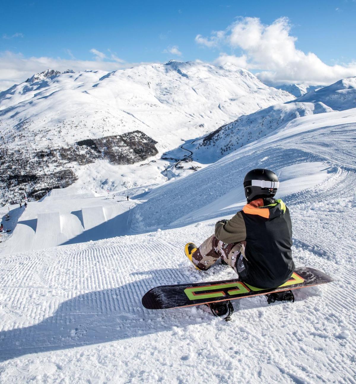 A person sat on a ski board at the top of a snowy mountain