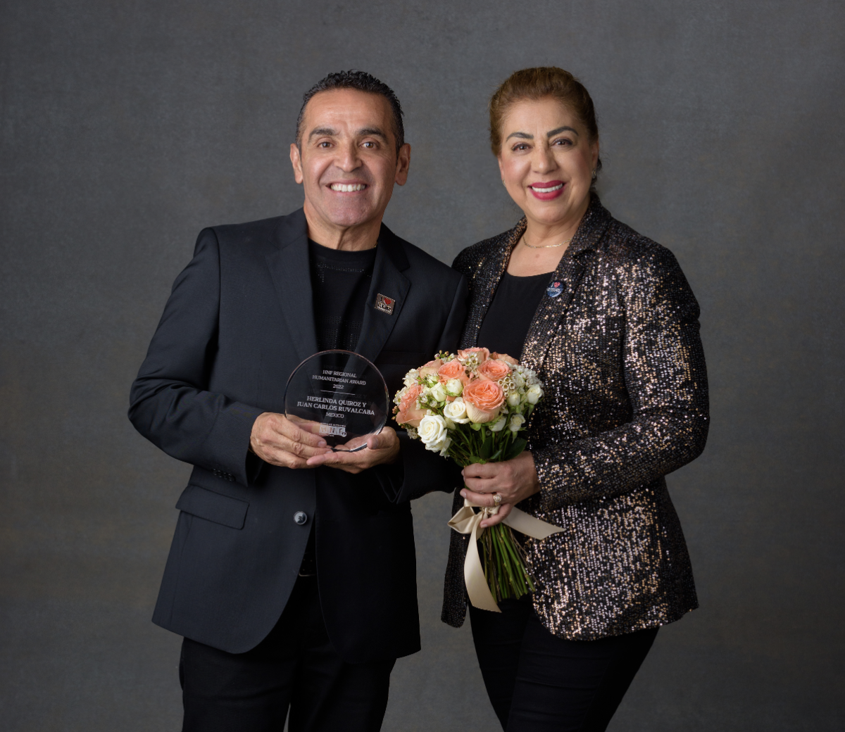 Two people stood next to each other smiling, one person holding an award and the other holding flowers