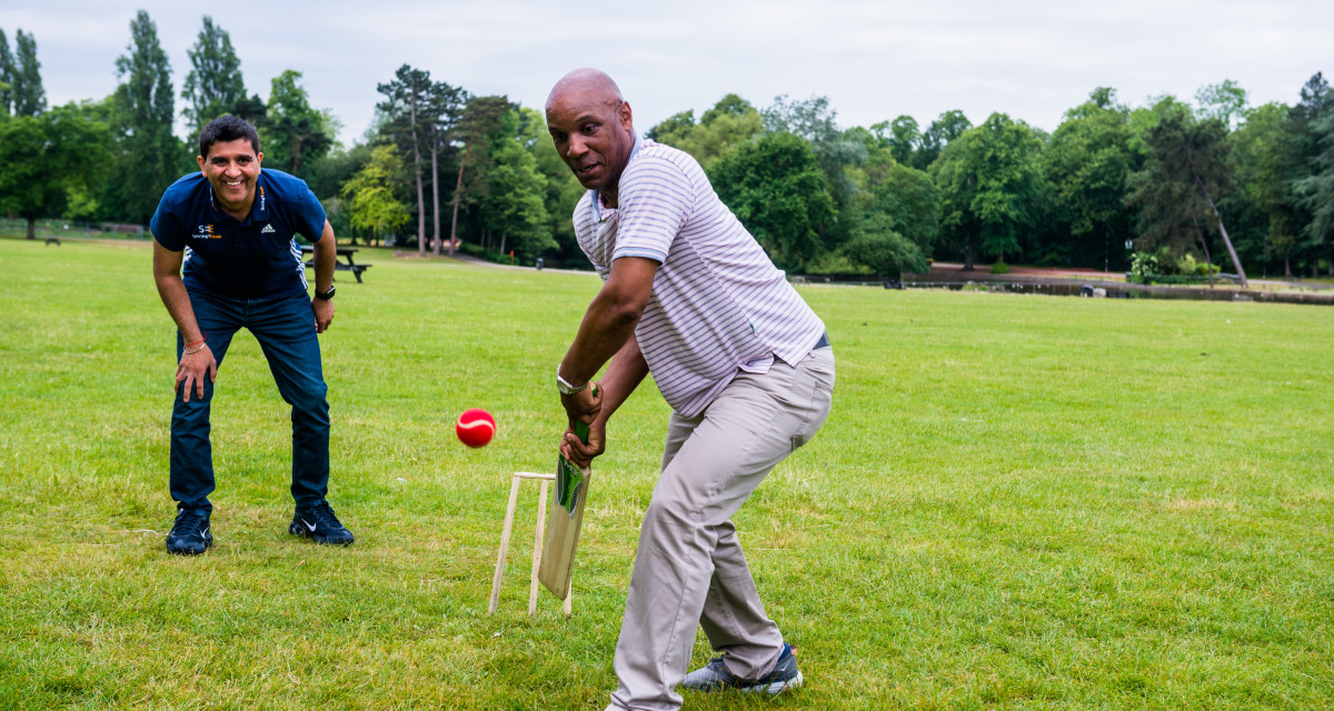 A black man playing cricket on a grassy field