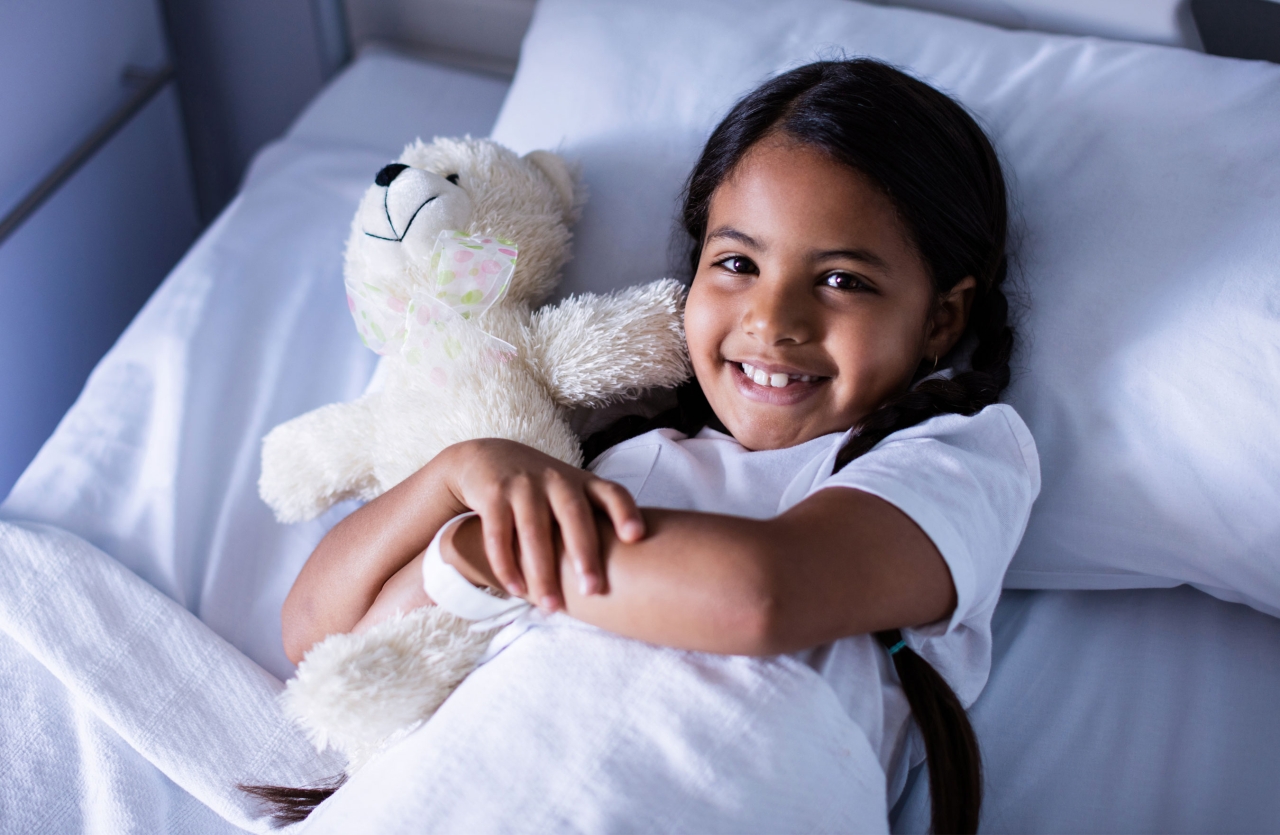 girl in hospital bed hugging teddy bear