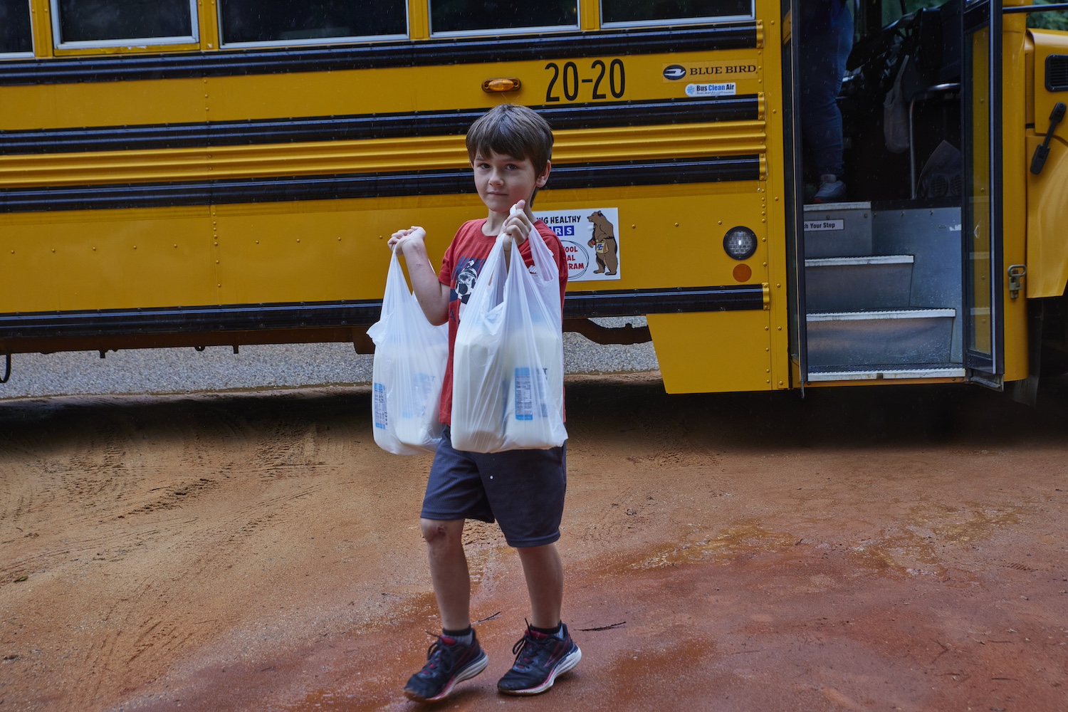 A young student collects food from the summer meals program, delivered on a school bus.