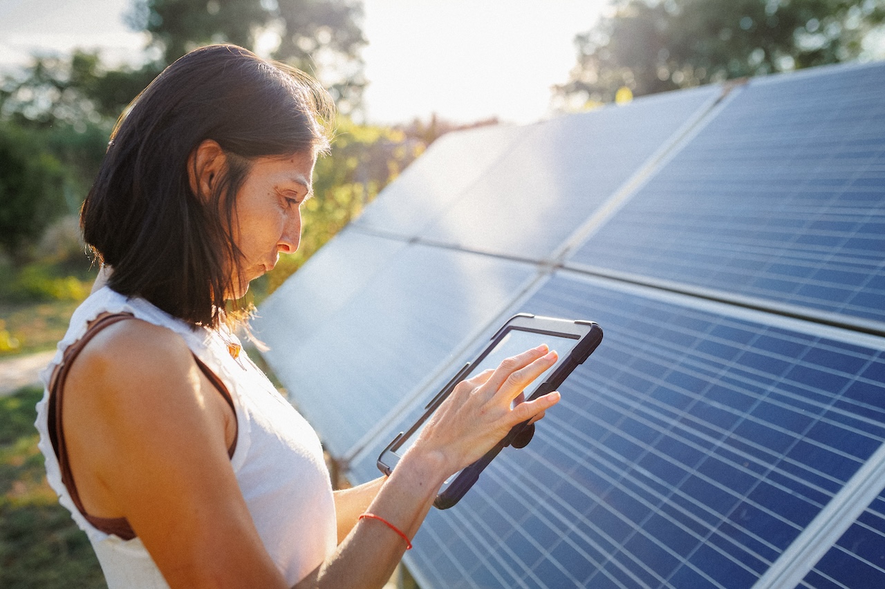 Woman holding a tablet and standing in front of a solar panel array.