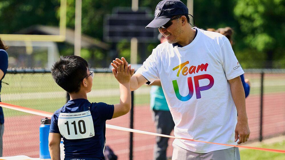 An adult wearing a Team UP shirt helping an athlete.