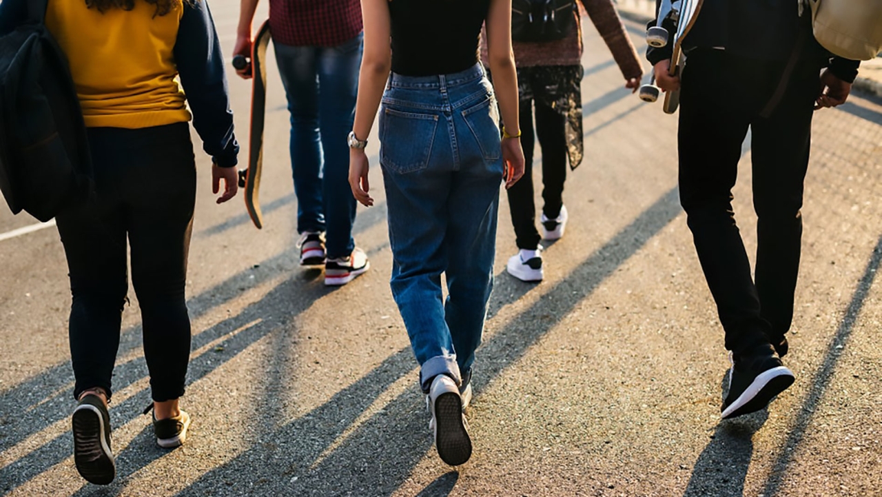young people in casual clothes, casting long shadows and walking away from the camera