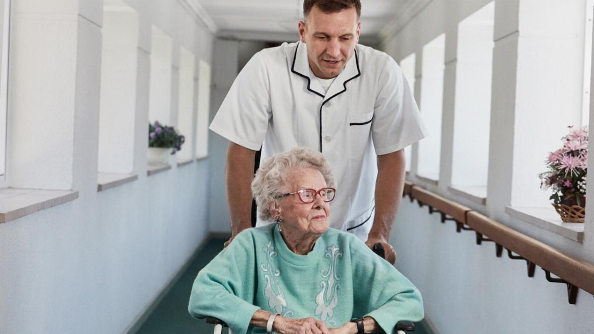Elderly woman being assisted in a wheelchair by a health care professional.