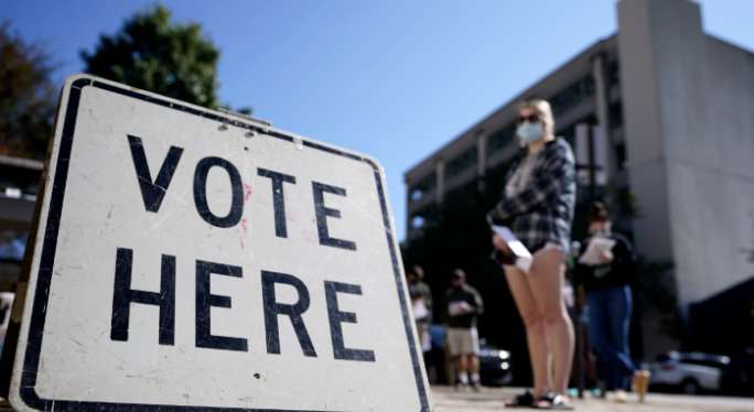 person stands if front of a Vote Here sign.