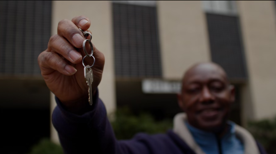 Black man holding a key in front of an apartment building.