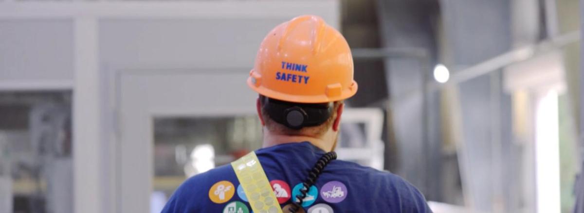 A person walking away, "Think Safety" on the back of their hard hat.