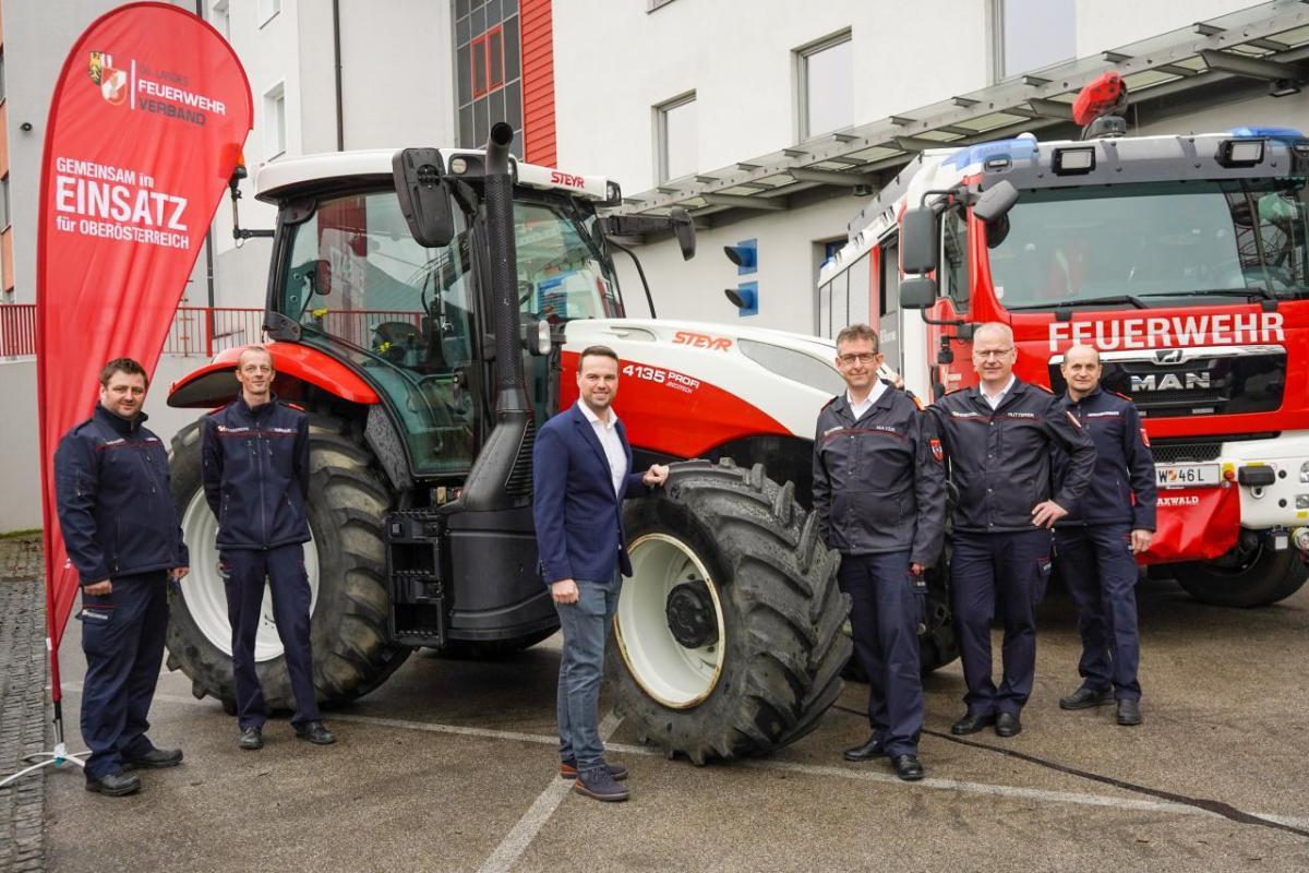 Six people stand arounf a large tractor and fire truck outside.