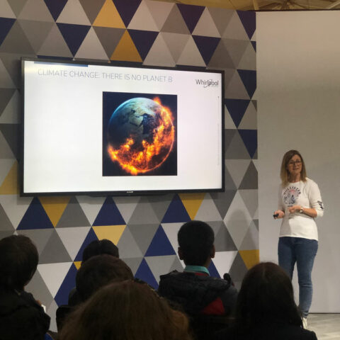 a person presenting to a small group of seated people. A monitor to their right showing the earth half engulfed in flames " There is no planet B"