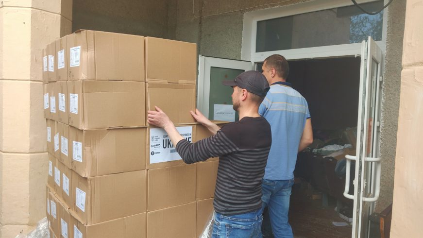 two people moving stacks of boxes inside open doors of a building