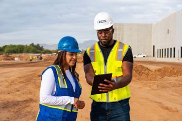 two workers on a construction site using a device 