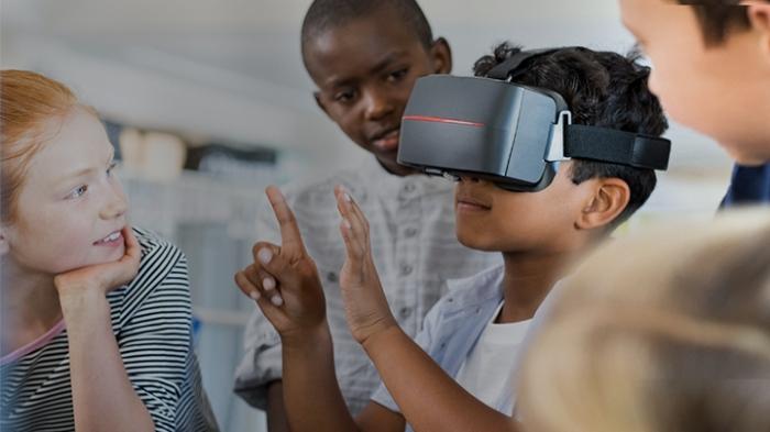 Children watch as another uses a VR headset.