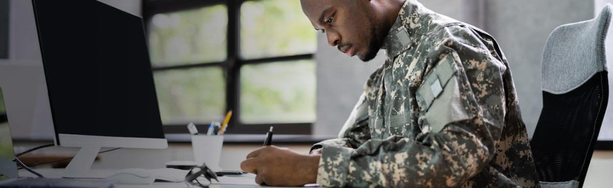 Male military individual seated at a desk wearing fatigues.