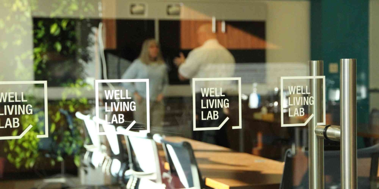 looking into the Well Living Lab from outside glass walls, two people talking inside