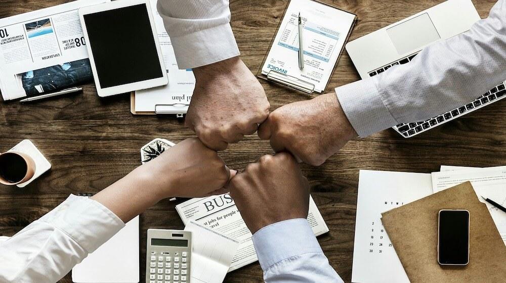 Four people fist bumping over a table at work.