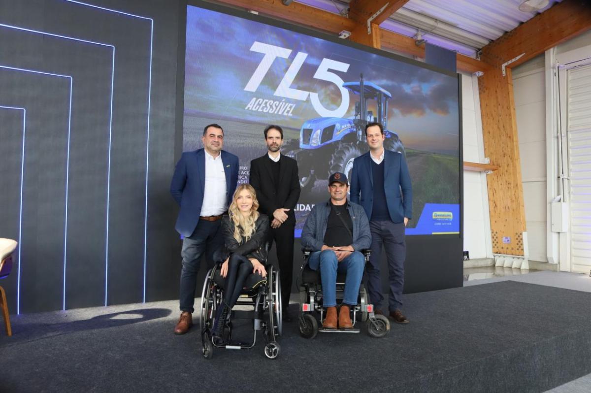 Three people standing behind two people in wheelchairs with a picture of the the Accessible New Holland TL5 tractor on the wall behind them