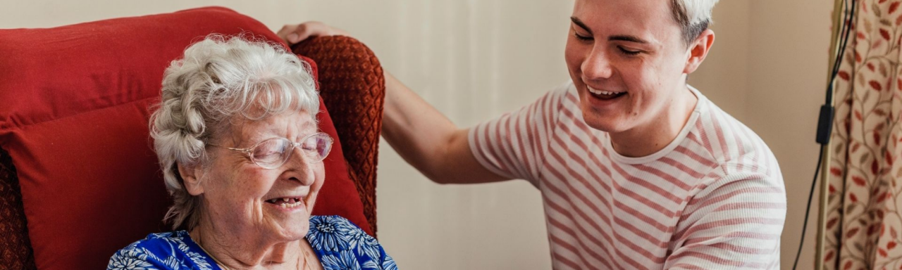 A volunteer laughing with an elderly woman in a red chair