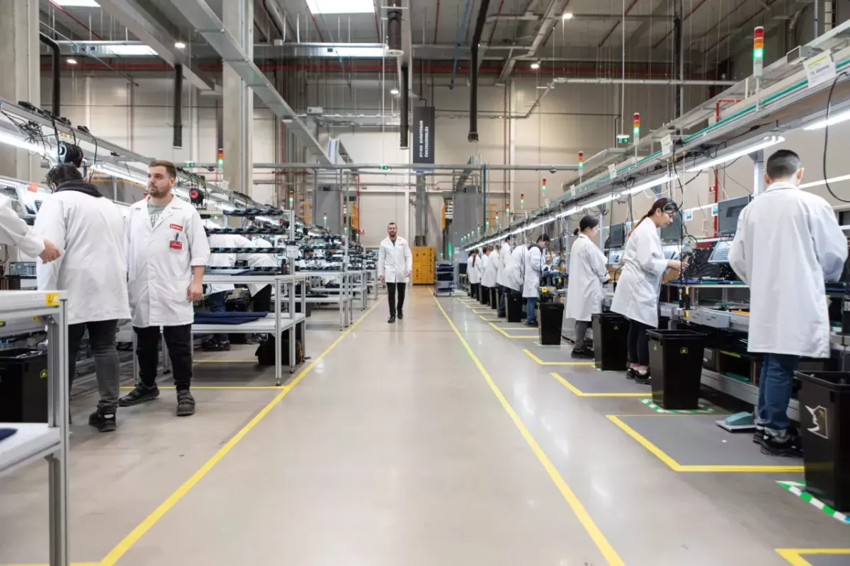 Long view at a manufacturing plant. People working on both sides of an aisle.