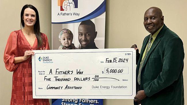 Two people holding a large check made out to "A Fathers Way"