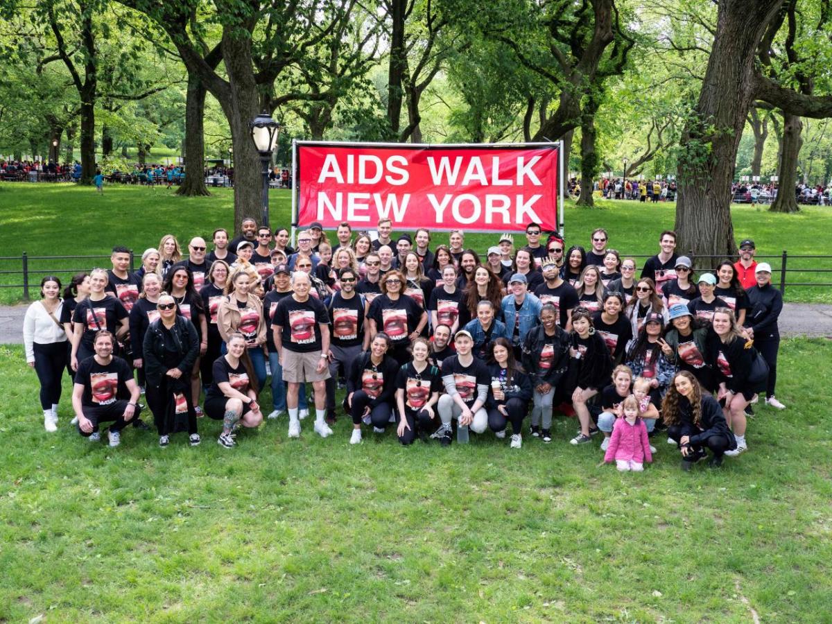 The MAC team of walkers in a park in front of "aids walk new york" sign.