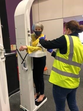 Alison demonstrating a “health pod,” used to monitor BMI and blood pressure, for the former Prime Minister of England, Theresa May. Photo taken by Diana Parott, practice manager of Maidenhead Vaccine Clinic, and provided by author.