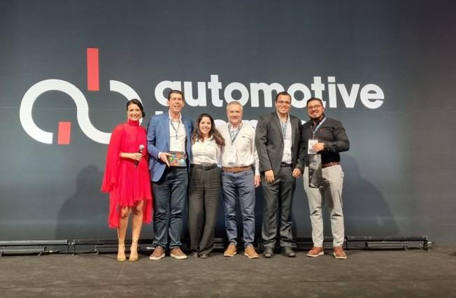 A row of people posed on a stage in front of a sign "Automotive". One holds an award.
