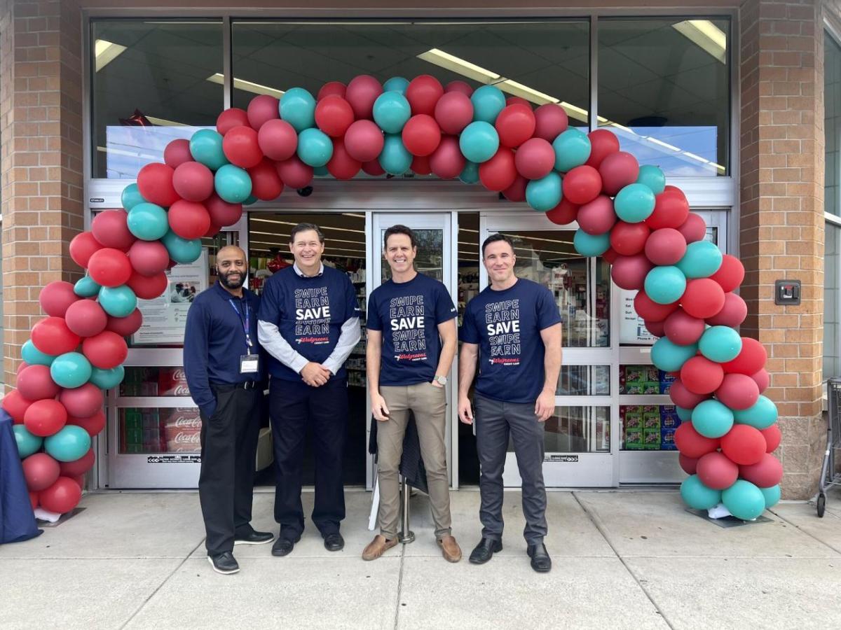 Four people posed outside a Walgreens. A balloon arch over the entrance.