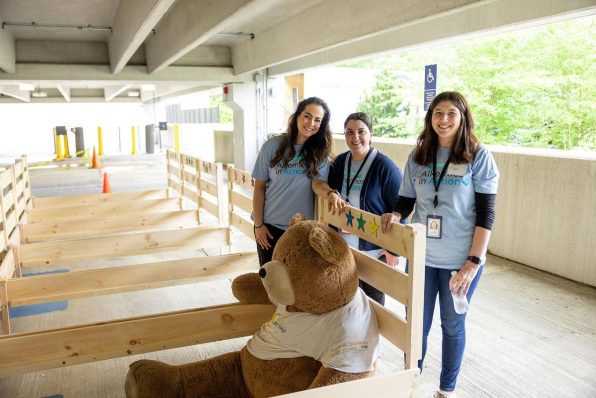 Three volunteers standing with a row of bed frames.