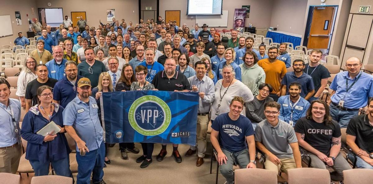 A large group posed in an auditorium. Some holding a VPP logo flag.