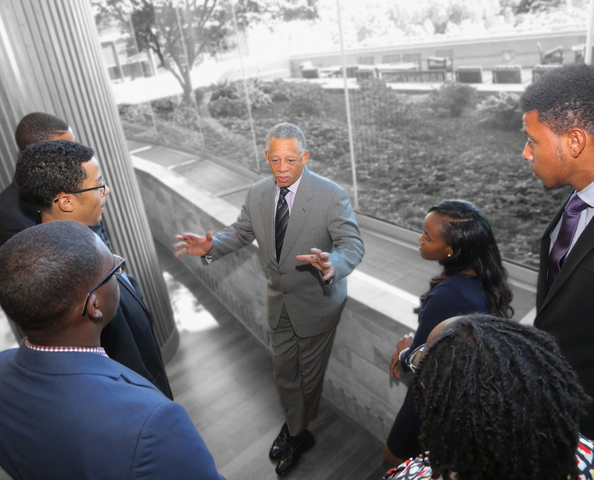 a group of people gather around one speaker in front of a wall of windows