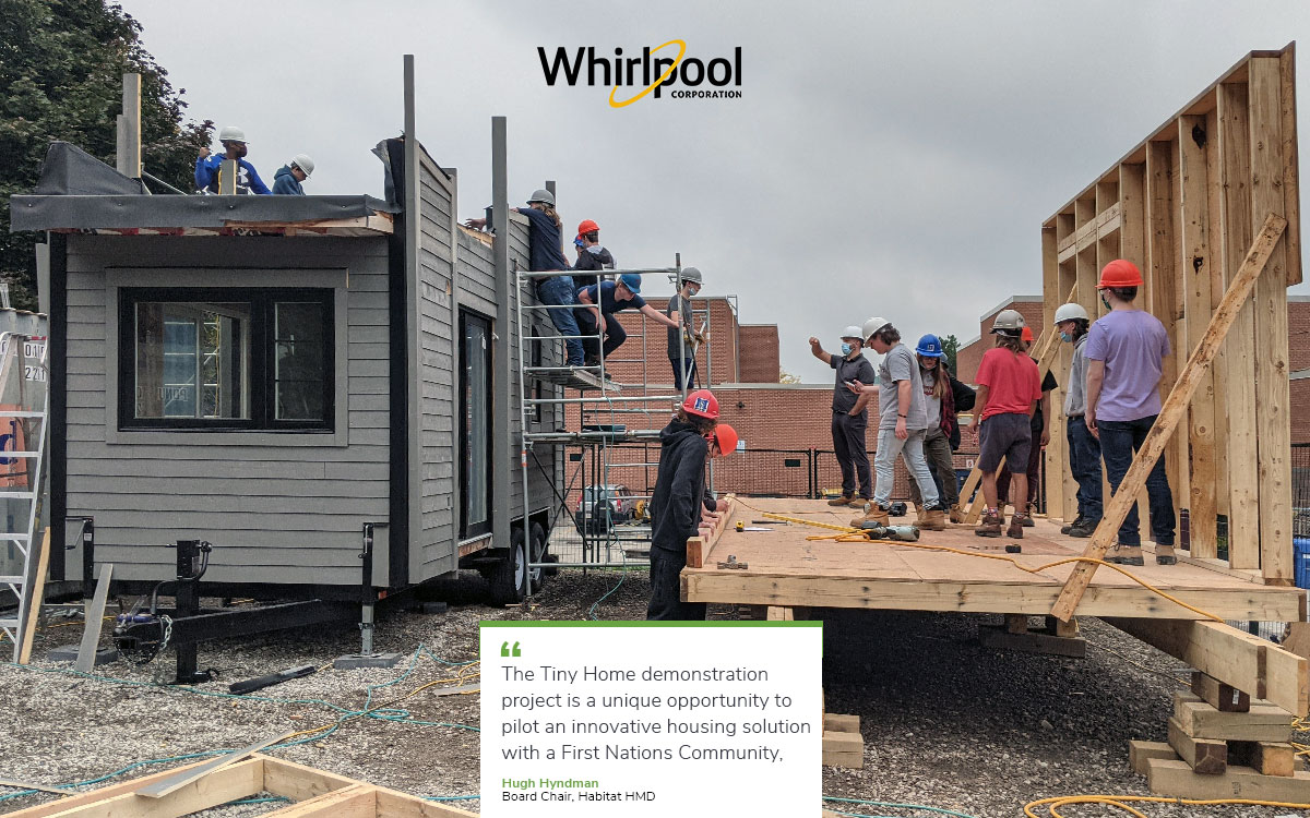 a group of people stand on wood building structure next to a completed tiny house