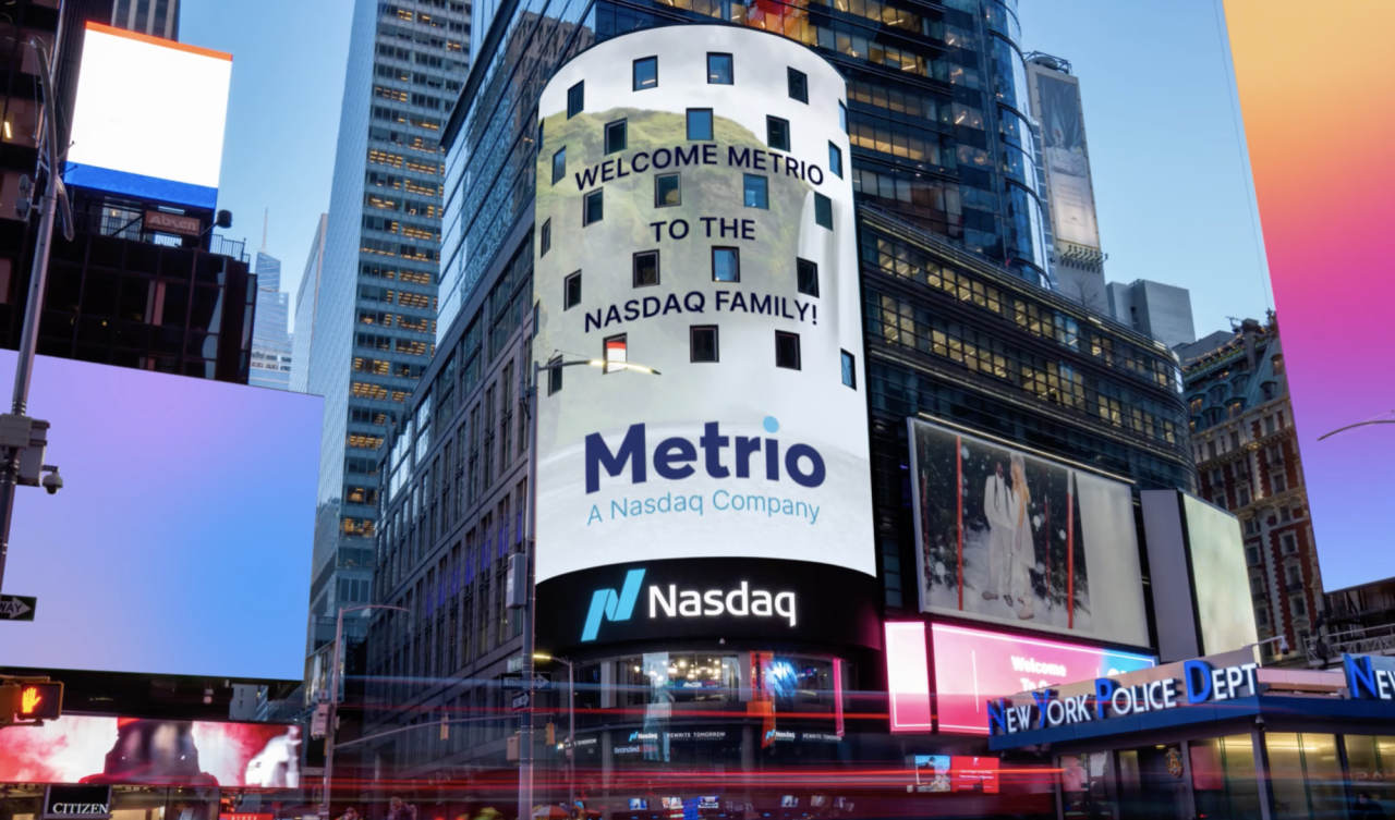 Billboard on the side of a tall building in a busy intersection. Metrio and Nasdaq logos.