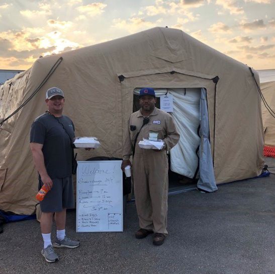 two people holding Styrofoam boxes and drinks outside a cloth tent