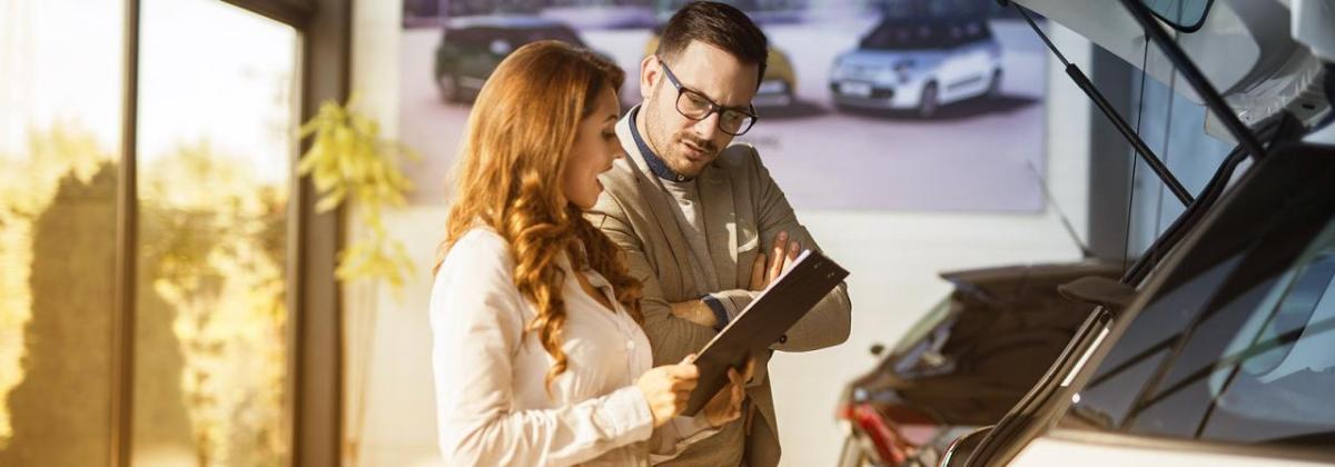 Two people in a car dealership looking at a clipboard.