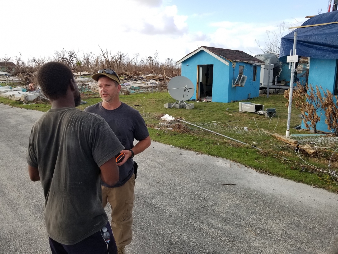 Two men talk outside buildings damaged by hurricanes